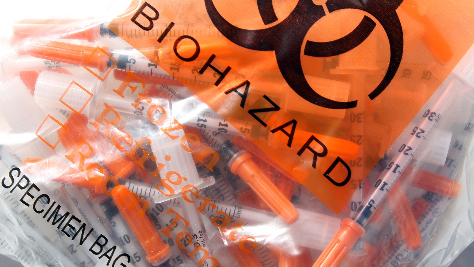 Medical waste bag with biohazard warning containing sharps.