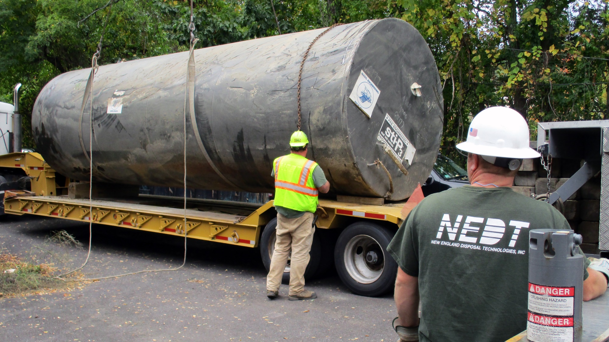 NEDT staff lower a large industrial tank onto a flatbed after tank removal.